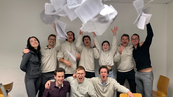 Eine Gruppe Studierender wirft Blätter in die Höhe und jubeln