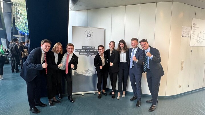 Eine Gruppe Studierender in Business-Kleidung jubelt.